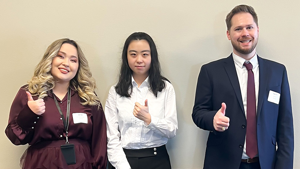 Three doctoral college students in business attire standing in a row and smiling.