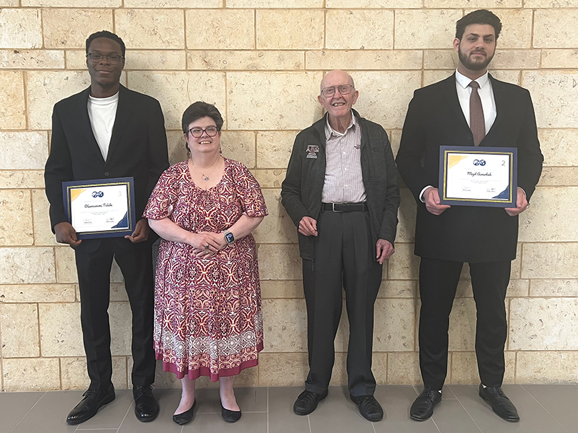 Two nicely-dressed master's students holding certificates and two faculty members from the Harold Vance Department of Petroleum Engineering at Texas A&M University stand in front of a wall.