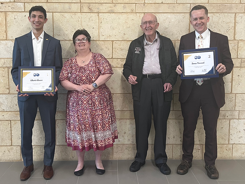 Two nicely-dressed undergraduate students holding certificates and two faculty members from the Harold Vance Department of Petroleum Engineering at Texas A&M University stand in front of a wall.