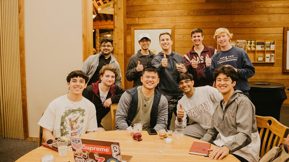 A group of male students gather around a table to pose for a photo while smiling. 