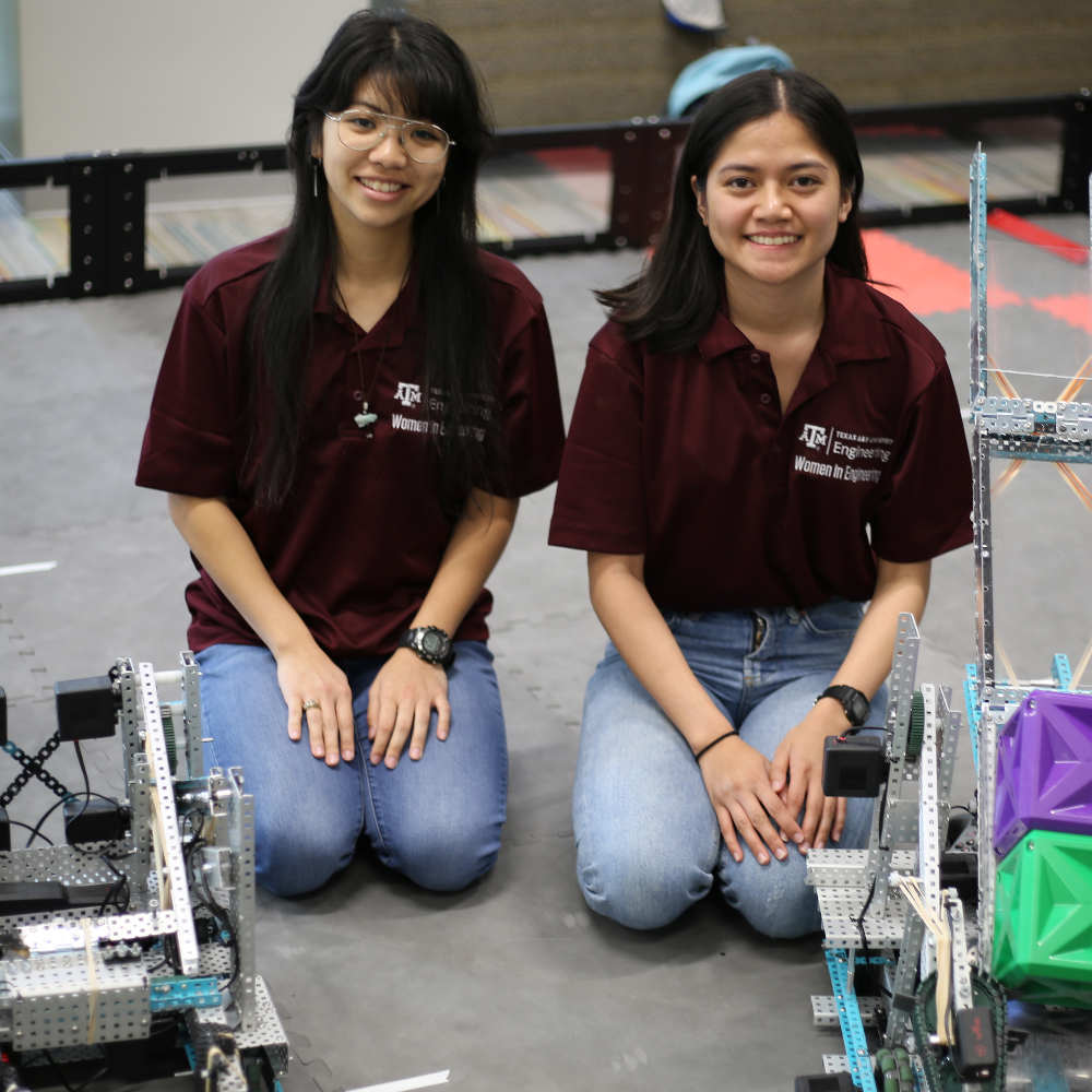 two women engineers sitting on ground behind two robots