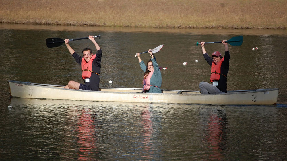Zachry Leadership Program students raise their paddles while sitting in a canoe